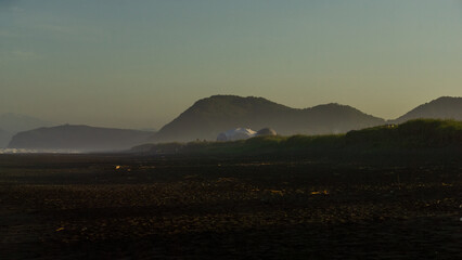Serene beach landscape at dusk, featuring gentle waves lapping against the shore, distant hills...