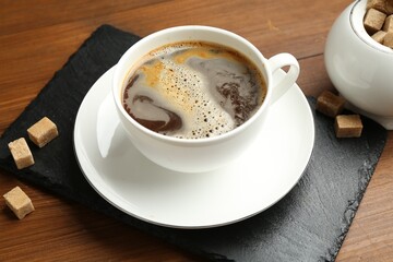 Tasty coffee in cup and sugar cubes on wooden table, closeup