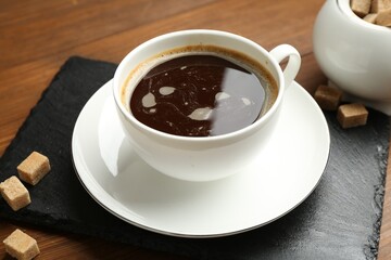Tasty coffee in cup and sugar cubes on wooden table, closeup
