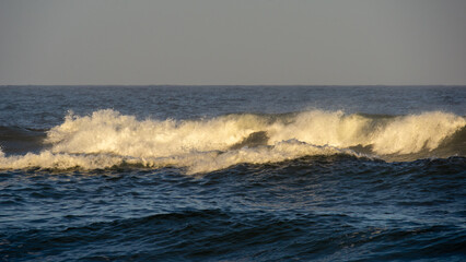 Ocean waves crashing against the shore, illuminated by golden sunlight, creating a serene and...