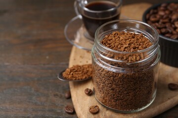Instant coffee in glass jar, hot drink and beans on wooden table, closeup. Space for text