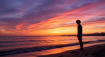 Fototapeta premium A person standing on the beach watching the sunset