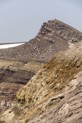 Rugged mountain landscape showcasing steep rocky cliffs and textured earth, with a distant peak...