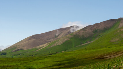 Majestic green hills under a clear blue sky, with gentle slopes and distant mountains, showcasing...