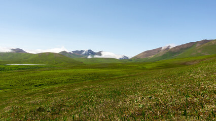 Expansive green landscape with rolling hills, distant mountains shrouded in clouds, and a serene...