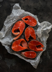 Pieces of fresh raw salmon on paper on a dark background, top view