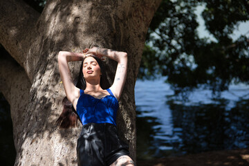 Young woman, dark-haired, tall, slim and very tattooed, wearing a blue top and leather shorts,...