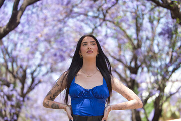 Young woman, brunette, tall, slim and heavily tattooed, wearing a blue top and short leather pants,...