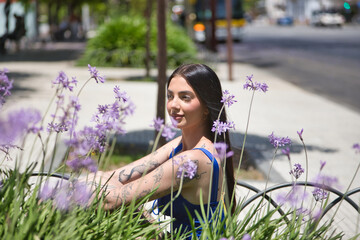 Portrait of a young woman, dark-haired, tall, slim, and very tattooed, wearing a blue top, looking...