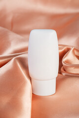 Cosmetic product in tube, bottle, lotion or serum on shiny cloth background