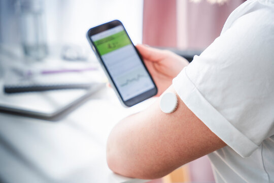 Woman using smartphone to monitor blood sugar levels with a wearable sensor