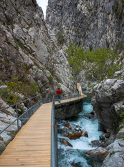 Wooden walkway in mountain gorge with lone person in red