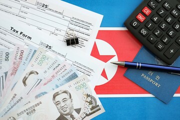 North Korean won money bills lies on table with pen, calculator, passport and tax forms