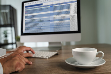 Man working on excel person working desk with computer and coffee cup, modern office environment, with blurred background, showing busy schedule