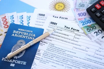 Argentine pesos money bills in big amount lies on table with pen, calculator, passport and tax forms
