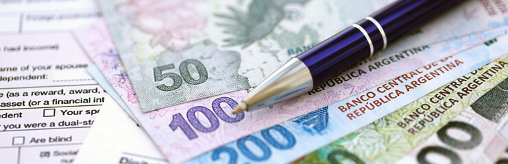 Argentine pesos money bills in big amount lies on table with pen and tax forms close up