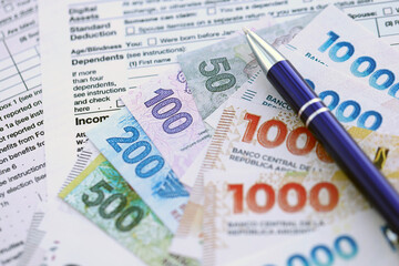 Argentine pesos money bills in big amount lies on table with pen and tax forms close up