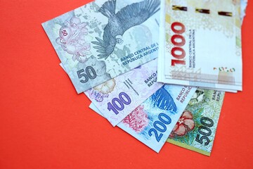 Argentine pesos money bills in big amount lies on red color table close up