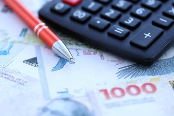 Argentine pesos money bills in big amount lies on table with pen and calculator close up