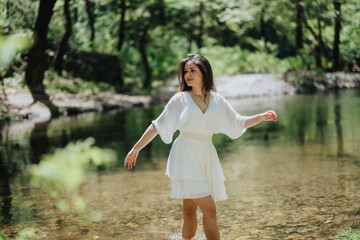 A young woman in a white dress enjoying a serene moment in a forest stream. The natural...