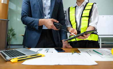 Construction manager and engineer discuss floor plan and project safety with tablet and blueprints....