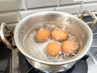 Four Brown Eggs Boiling in a Silver Pot on Gas Stove in Kitchen