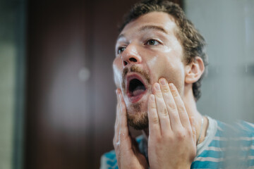 A young man invigoratingly washing his face with water in a bathroom, displaying a morning grooming...