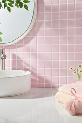 White sink with chrome faucet placed against a pink tiled wall, soft towel and floral accents....