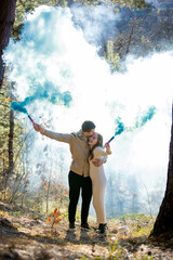 Cheerful joyfully celebrating their pregnancy couple surrounded by blue smoke in a beautiful, lush...