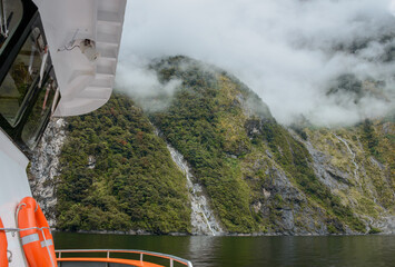 Boat cruising Milford Sound. Southern Rata forest blooming with red flowers. Fiordland National Park. South Island. New Zealand.