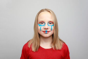 Smiling girl child with vibrant blue and red face paint makeup on her cheeks and forehead....