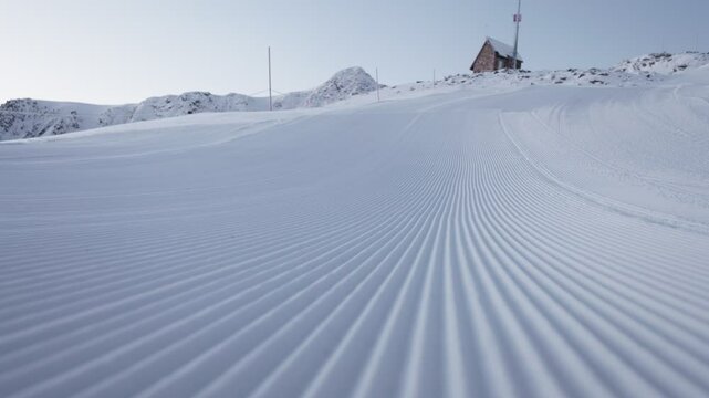 Side shot of fresh groomed snow slope with a mountain house in the background. Daylight scene in Andorra alpine area.