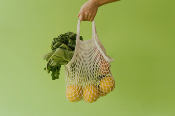 A minimalist product photography shot of a white mesh string bag against a solid lime green background
