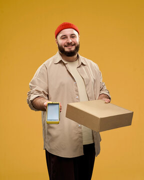 Smiling courier holding a package and smartphone in a studio portrait