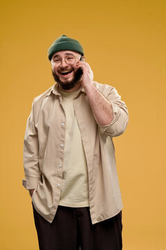 Smiling man wearing a beanie and glasses talking on the phone in a studio portrait