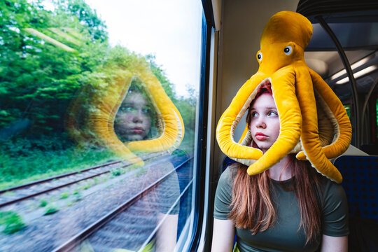 A thoughtful girl wearing an octopus hat on a train looking out the window