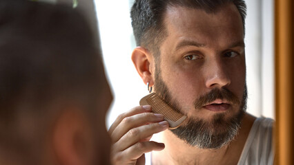 Clean-boy grooming. Man trims, styles his beard with focus and precision. Concept of personal...