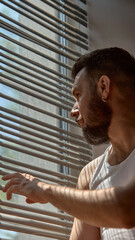 Glam shadows. Man sits in partial light, shadow lines from blinds across his face. Concept of...