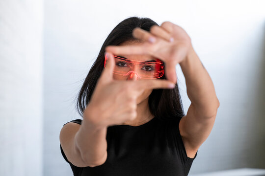 Young woman wearing AR glasses framing with hands indoors