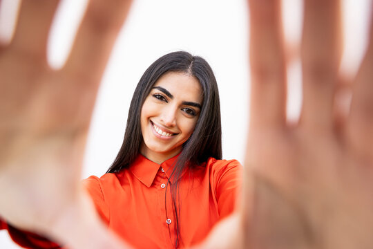 Confident woman in orange shirt smiling and framing with hands against white wall