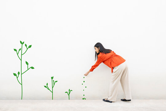 Person in orange shirt interacting with plant illustrations on a white wall indoors