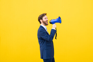Businessman with megaphone against yellow wall smiling