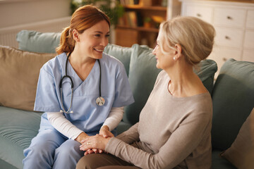 A smiling nurse in scrubs and a stethoscope provides care and support to a senior woman in her...