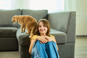 A calm moment unfolds in a cozy home as a teen girl sits on the floor, observing her Scottish Fold...