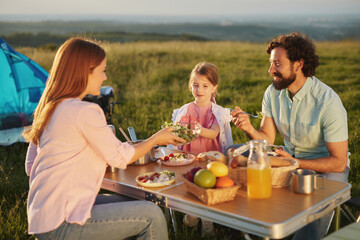 Family members gather at a picnic table, sharing a variety of delicious dishes while enjoying the beautiful sunset outdoors. Laughter and joy fill the air in this tranquil setting.