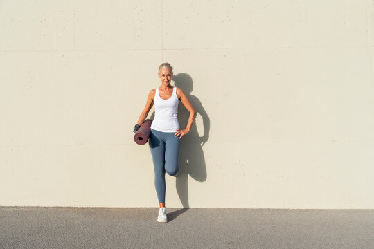 Woman with exercise mat leaning on cream colored wall