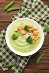 Tasty pea cream soup with croutons and broccoli served on wooden table, flat lay