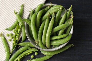 Fresh ripe green peas on black wooden table, flat lay