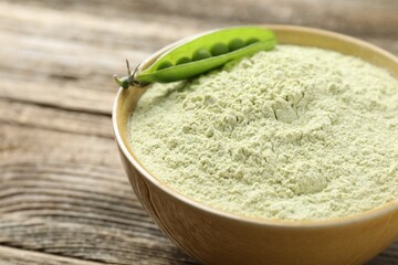 Protein powder and fresh pea pod on wooden table, closeup