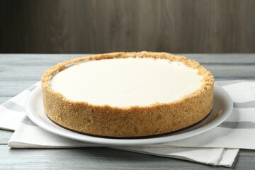 One tasty cheesecake on grey wooden table against brown background, closeup